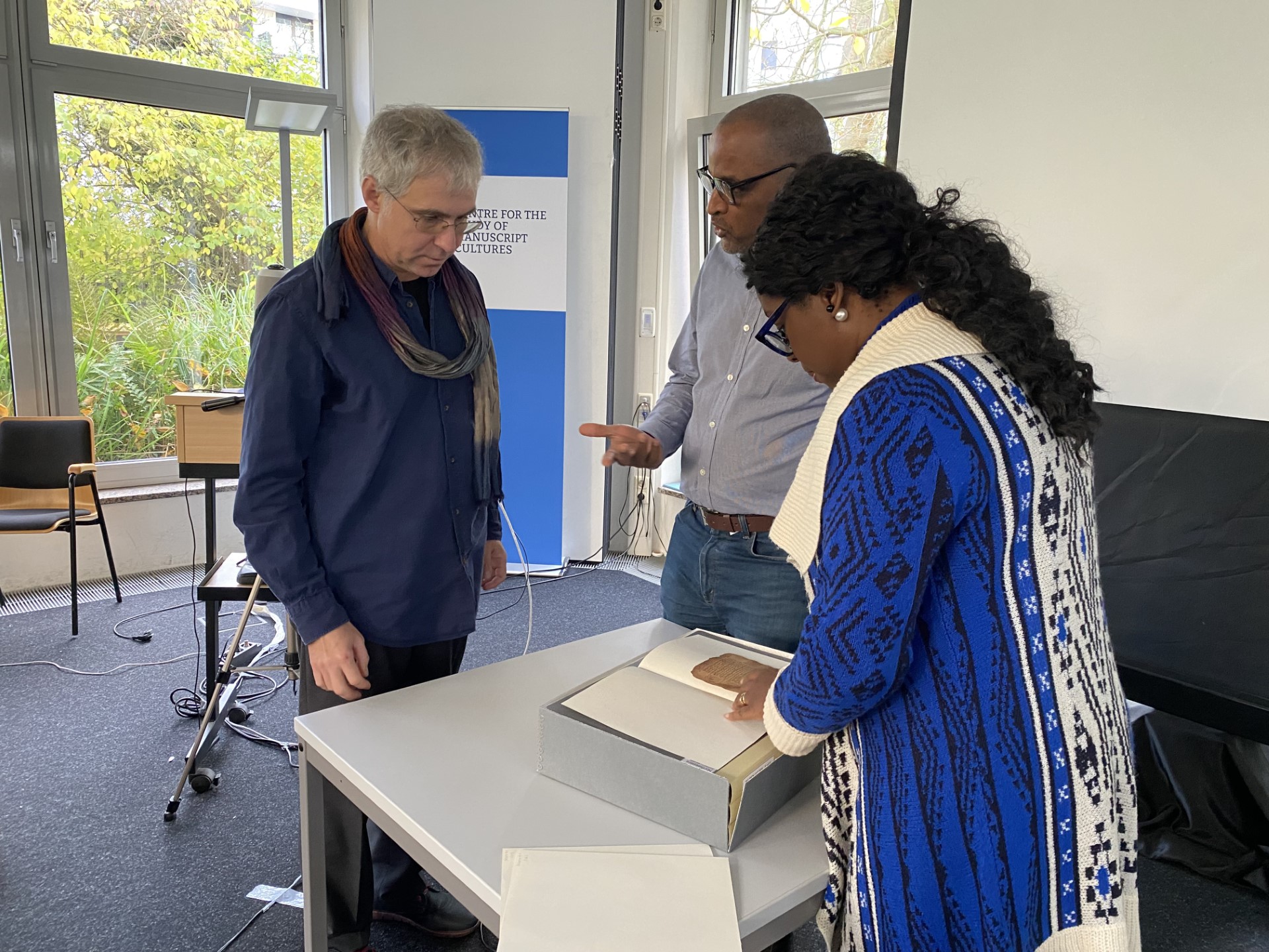 Three people gather around a table, looking at and discussing a manuscript.